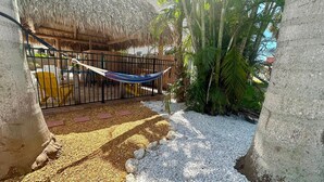 A hammock tied between two trees, a thatched-roof structure, and a paved pathway with palm trees. - The Turtle Nest 8 in Fort Myers Beach (Fort Myers Beach)