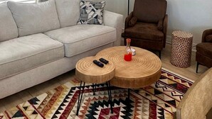 A living room with a sofa, armchair, round wooden coffee table, patterned rug, and wall art. - The Turtle Nest 8 in Fort Myers Beach (Fort Myers Beach)