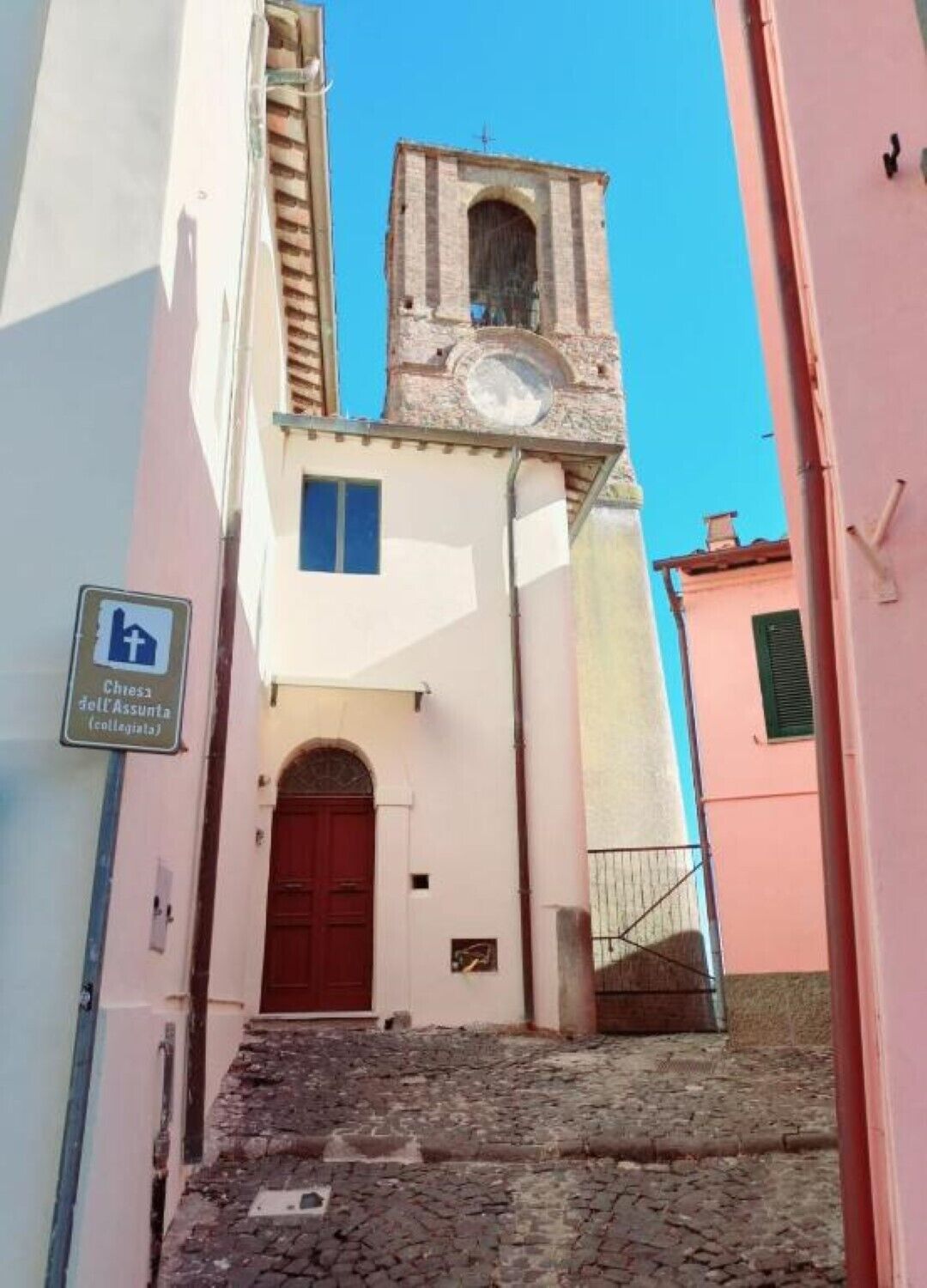 Una calle estrecha con una escalera de piedra que lleva a un edificio con puerta roja y una torre del reloj.