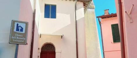Una calle estrecha con una escalera de piedra que lleva a un edificio con puerta roja y una torre del reloj.