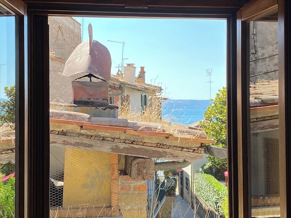 A view through a window of a building with a stone structure, a chimney, and a view of the sea.