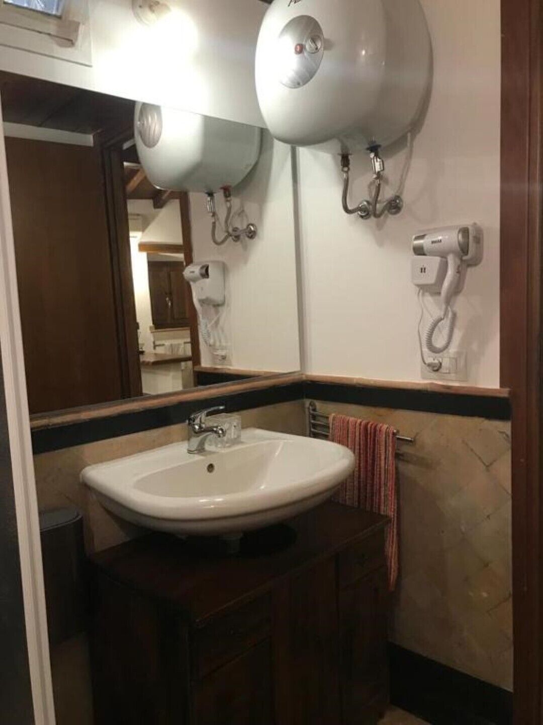 Une salle de bain avec un lavabo blanc, un miroir et deux sèche-cheveux fixés au mur.