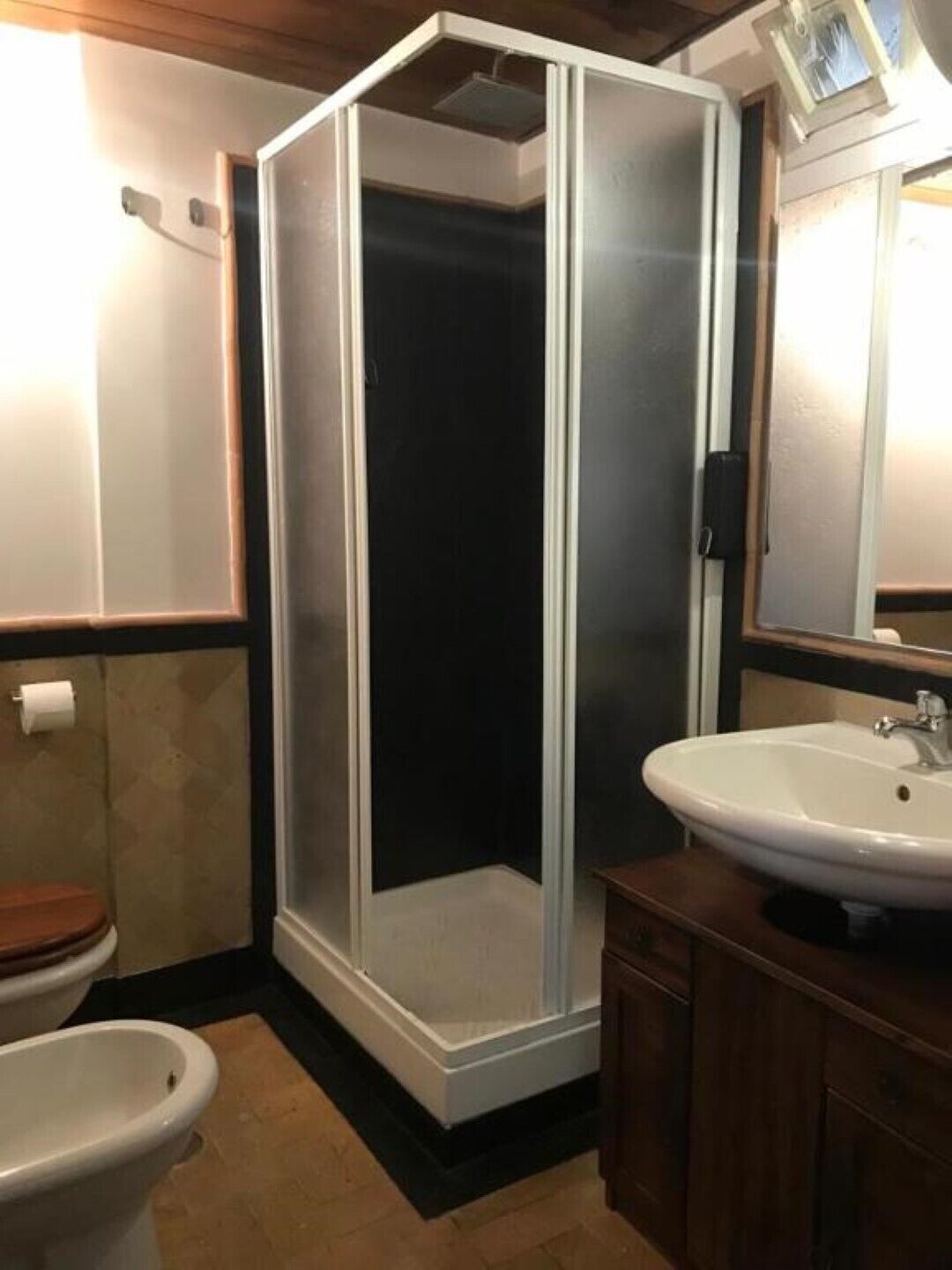 A bathroom with a shower enclosure, a toilet, a sink, and a mirror.