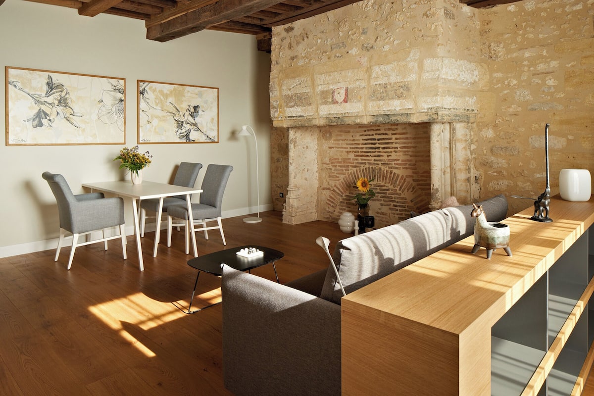 A modern living room with a wooden ceiling, a fireplace, and a dining area with chairs and a table.