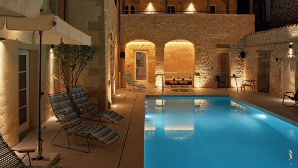 A pool area with lounge chairs and a stone building in the background. - Hotel Le Chevalier Bleu (Monpazier)