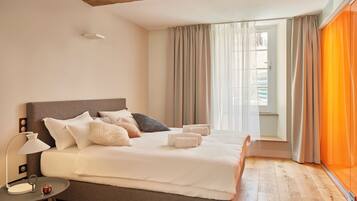 A modern bedroom with a large bed, a bedside table with a lamp, and a view of the outdoors through sheer curtains.