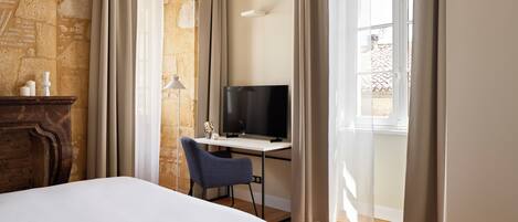 Habitación de hotel con cama, escritorio con televisor, silla y pared de piedra.