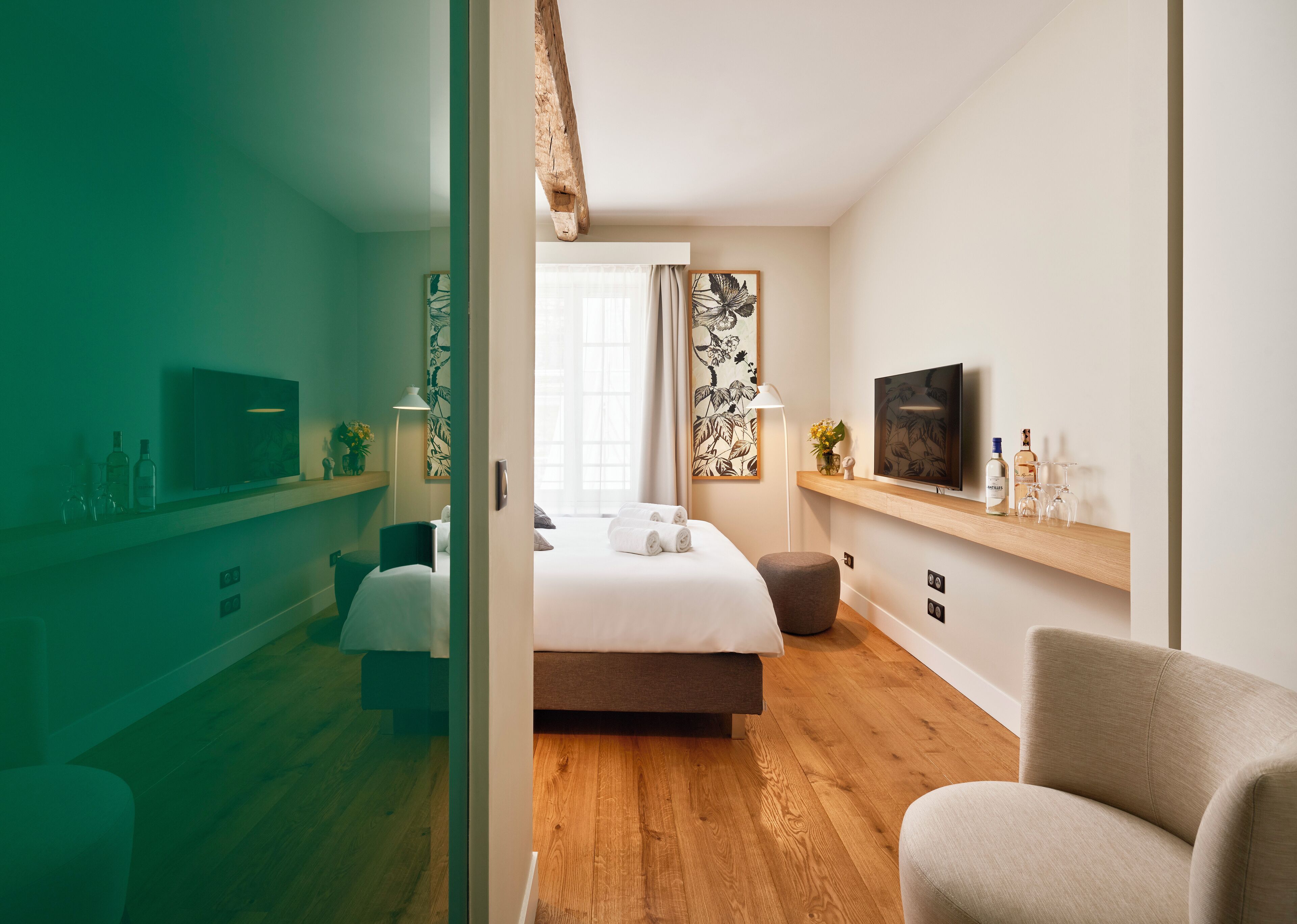 A modern hotel room with a bed, a TV, a seating area, and a wooden floor.