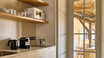 Una cocina moderna con estantes de madera, una cafetera y vistas a un área de estar exterior a través de un ventanal.