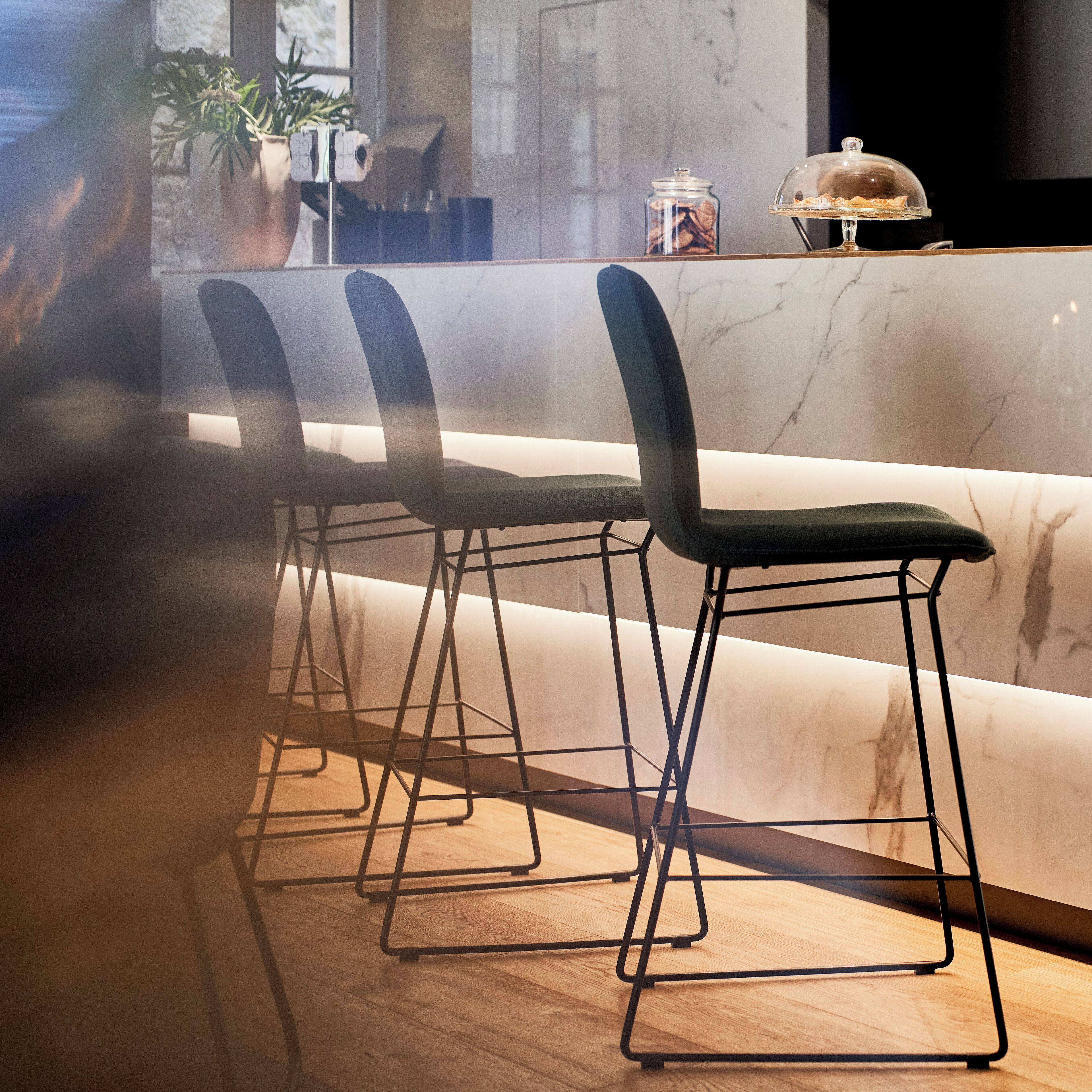 Un área de bar moderna con encimera de mármol, sillas de metal negro y suelo de madera.