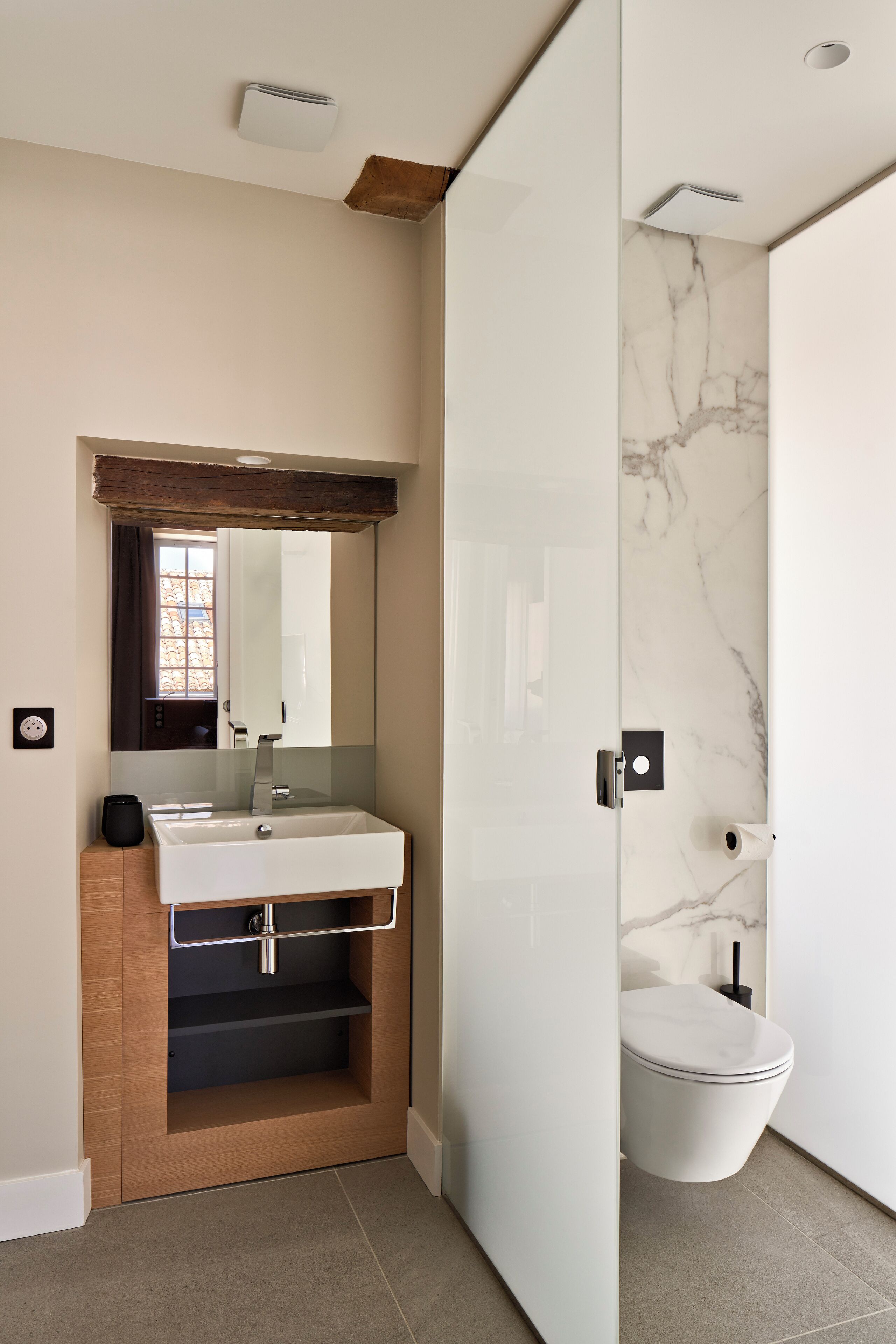 A modern bathroom with a wooden vanity, a large mirror, a marble backsplash, and a toilet.