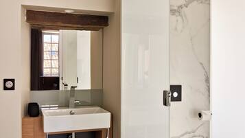 Un baño moderno con tocador de madera, un espejo grande, salpicadero de mármol y un inodoro.
