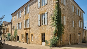 A stone building with multiple windows and a door, surrounded by cobblestone pavement. - Hotel Le Chevalier Bleu (Monpazier)