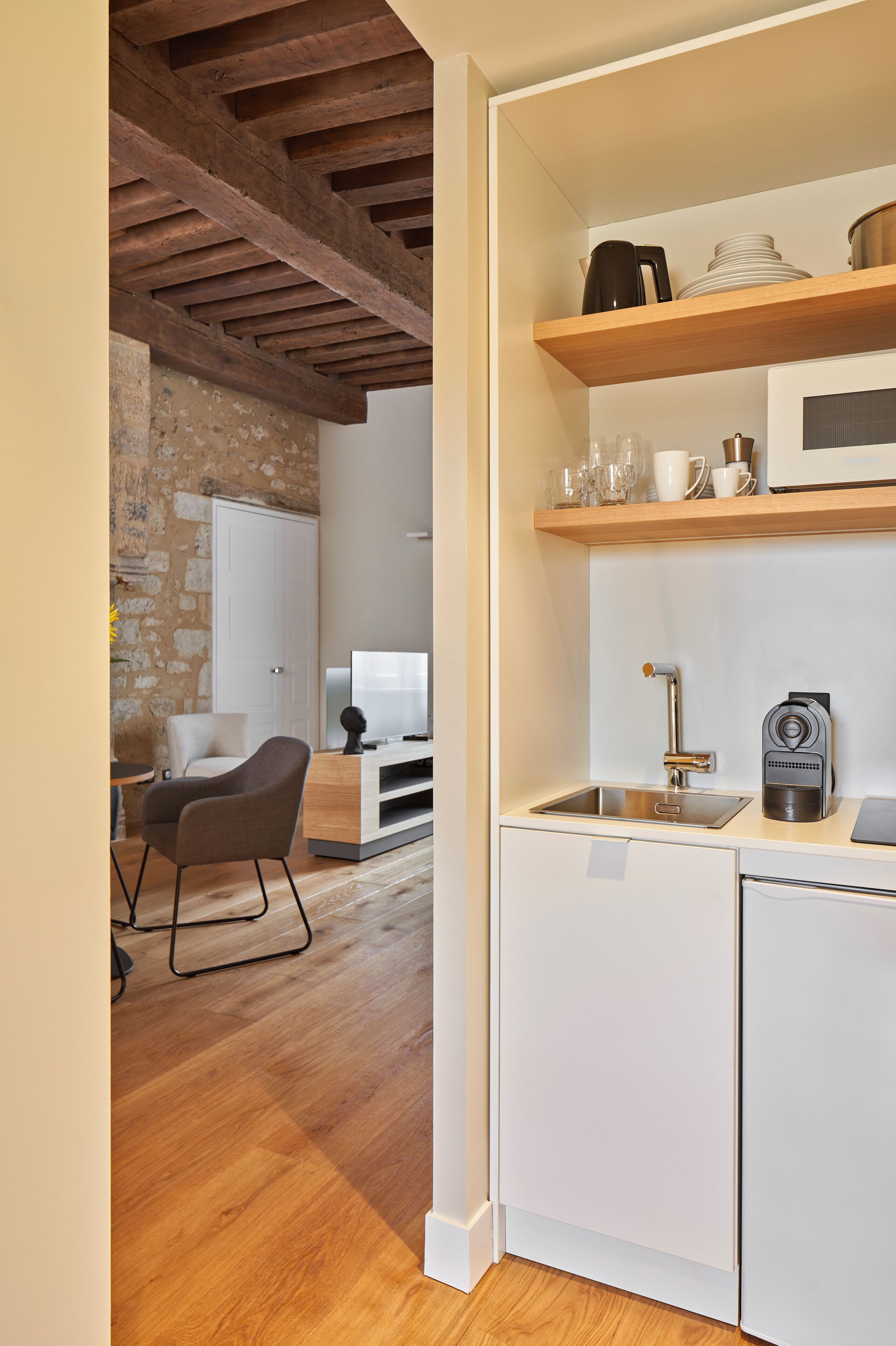 Una cocina moderna con armarios blancos, techo de madera y pared de piedra.