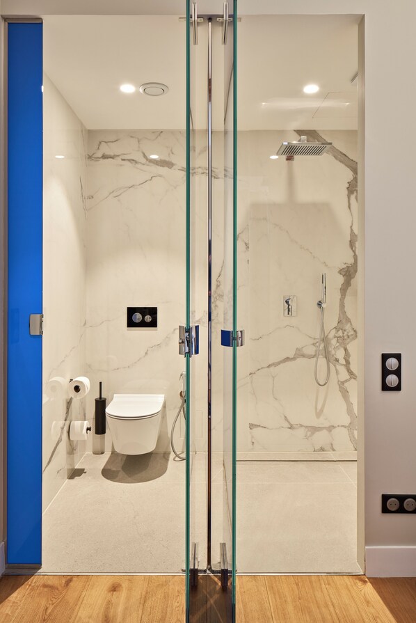 Un baño moderno con mampara de vidrio, pared de mármol, inodoro y zona de ducha.