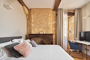 Quarto com cama, escrivaninha, cadeira, parede de pedra e lareira.