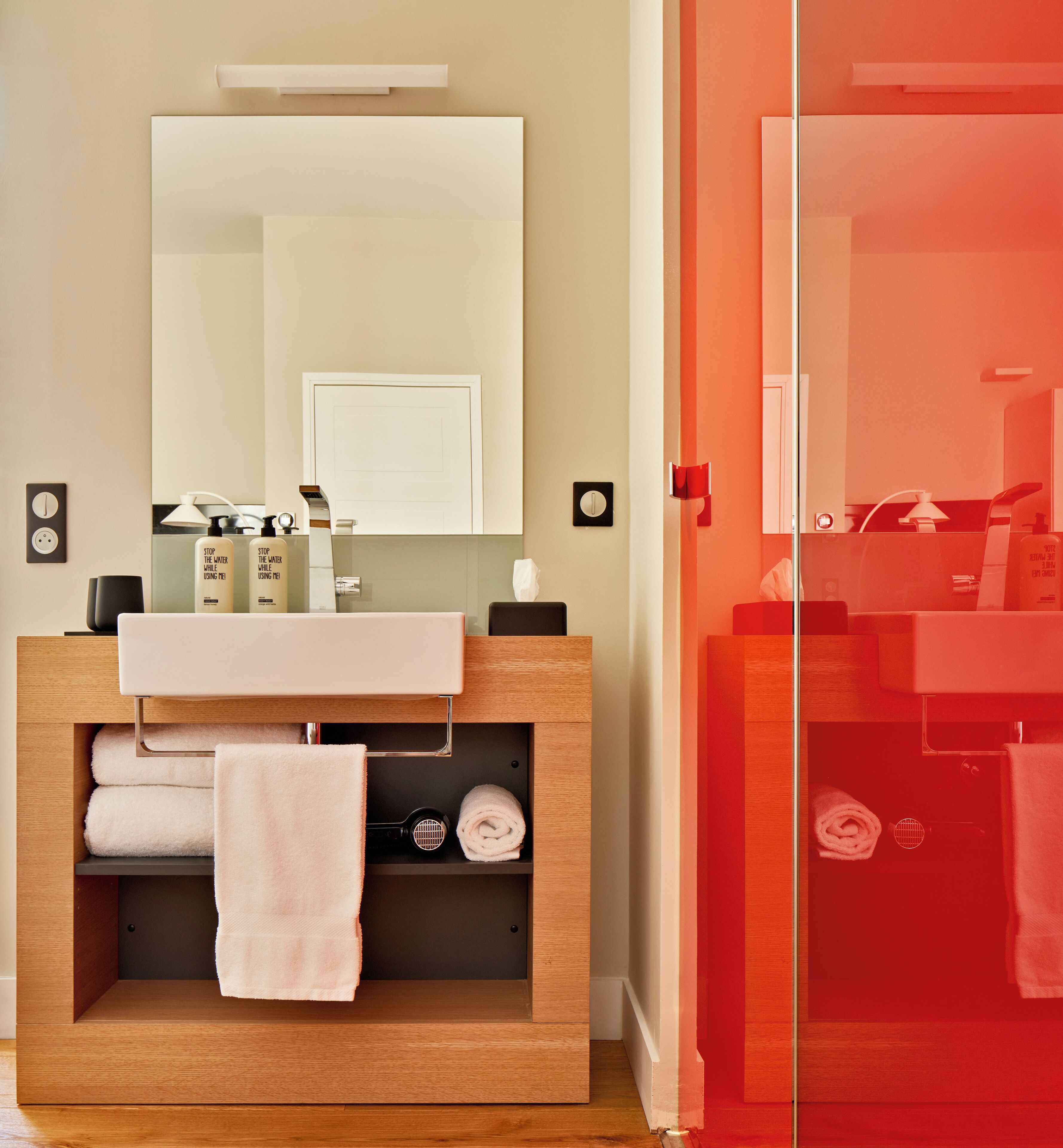 Une salle de bain avec un meuble-lavabo en bois, un miroir, un porte-serviettes et une cabine de douche en verre.