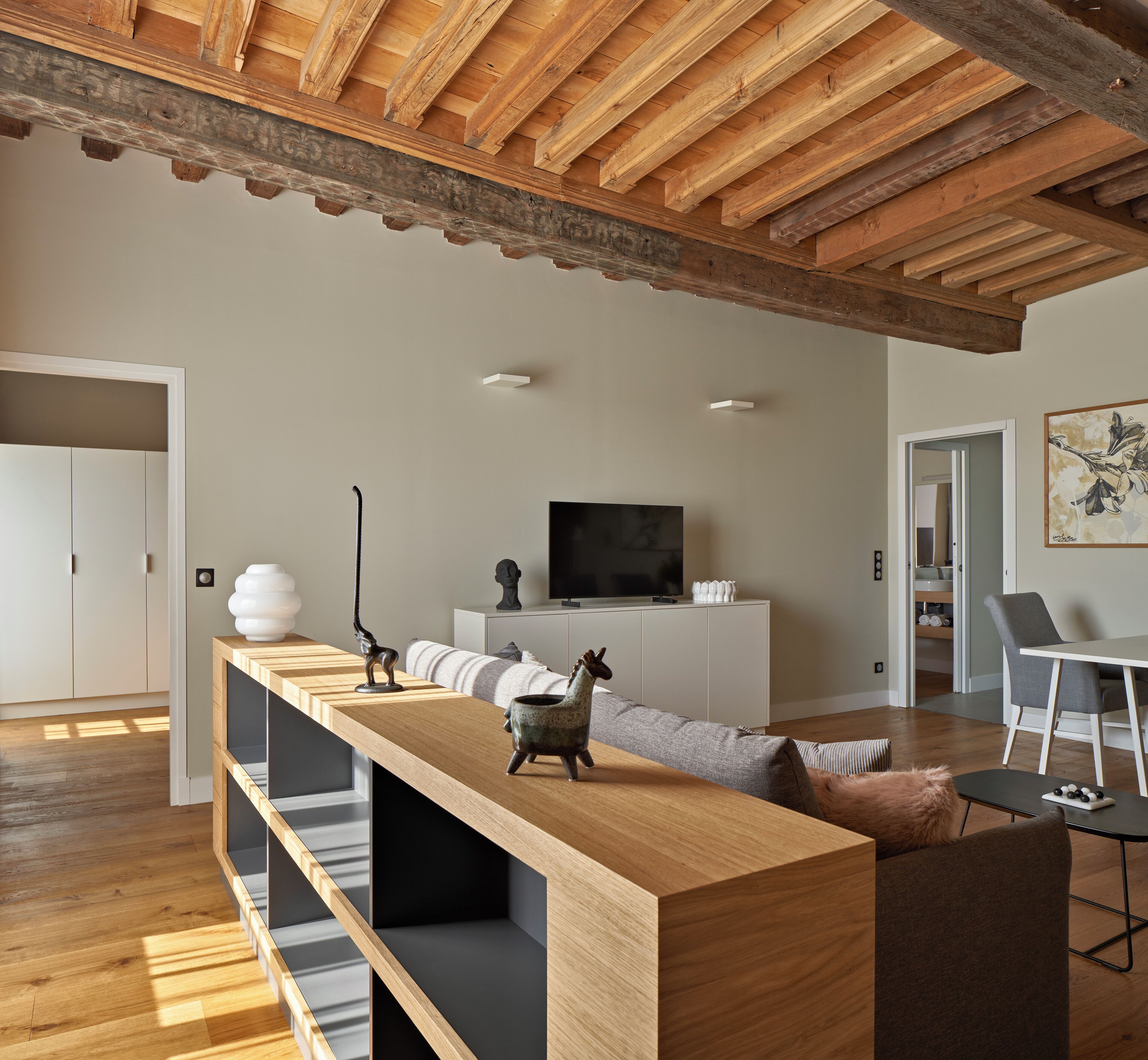 A modern living room with a wooden ceiling, a long wooden table, a sofa, a TV, and a dining area with chairs.