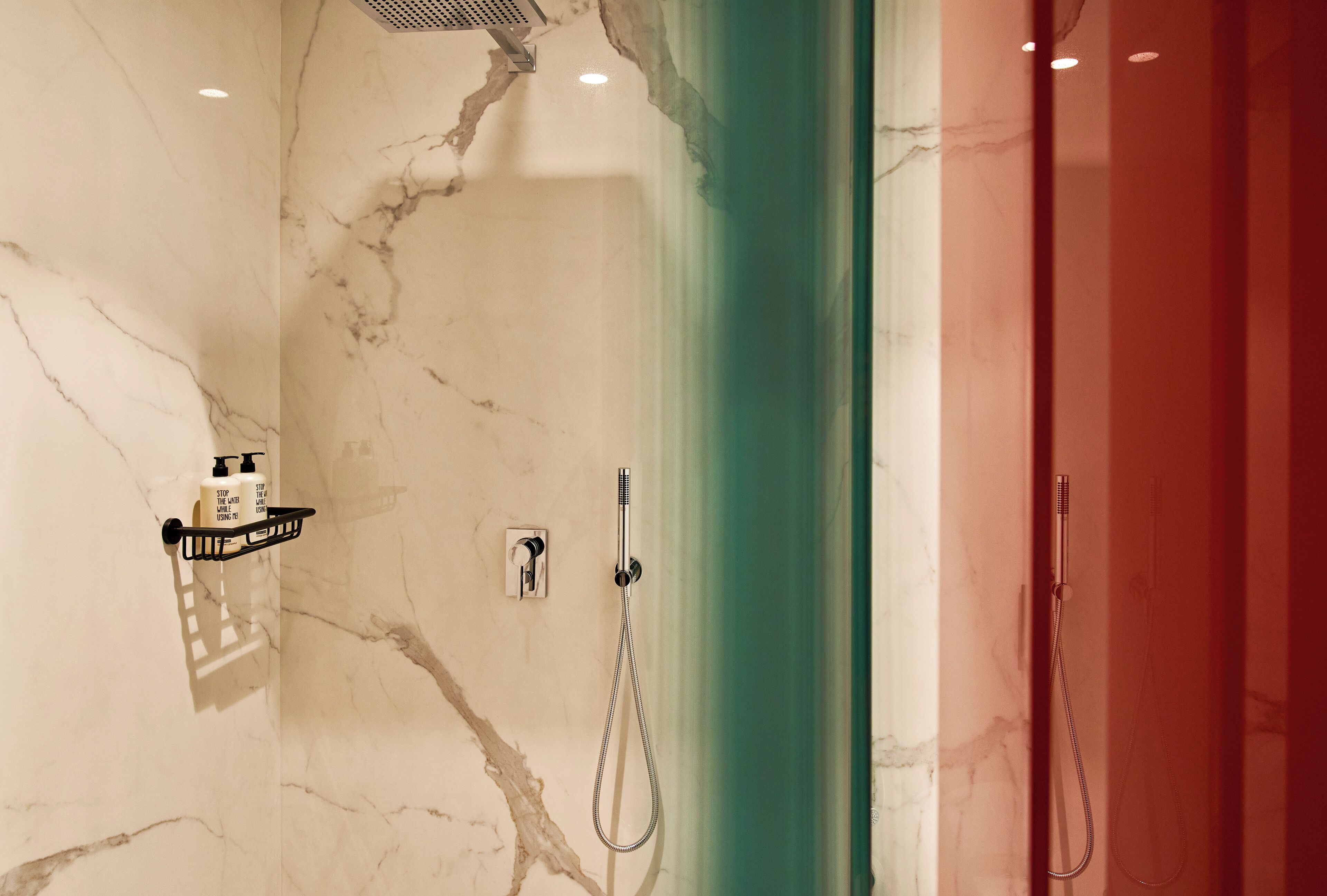 Un baño con pared de mármol, ducha con cabezal de ducha manual y cortina verde.