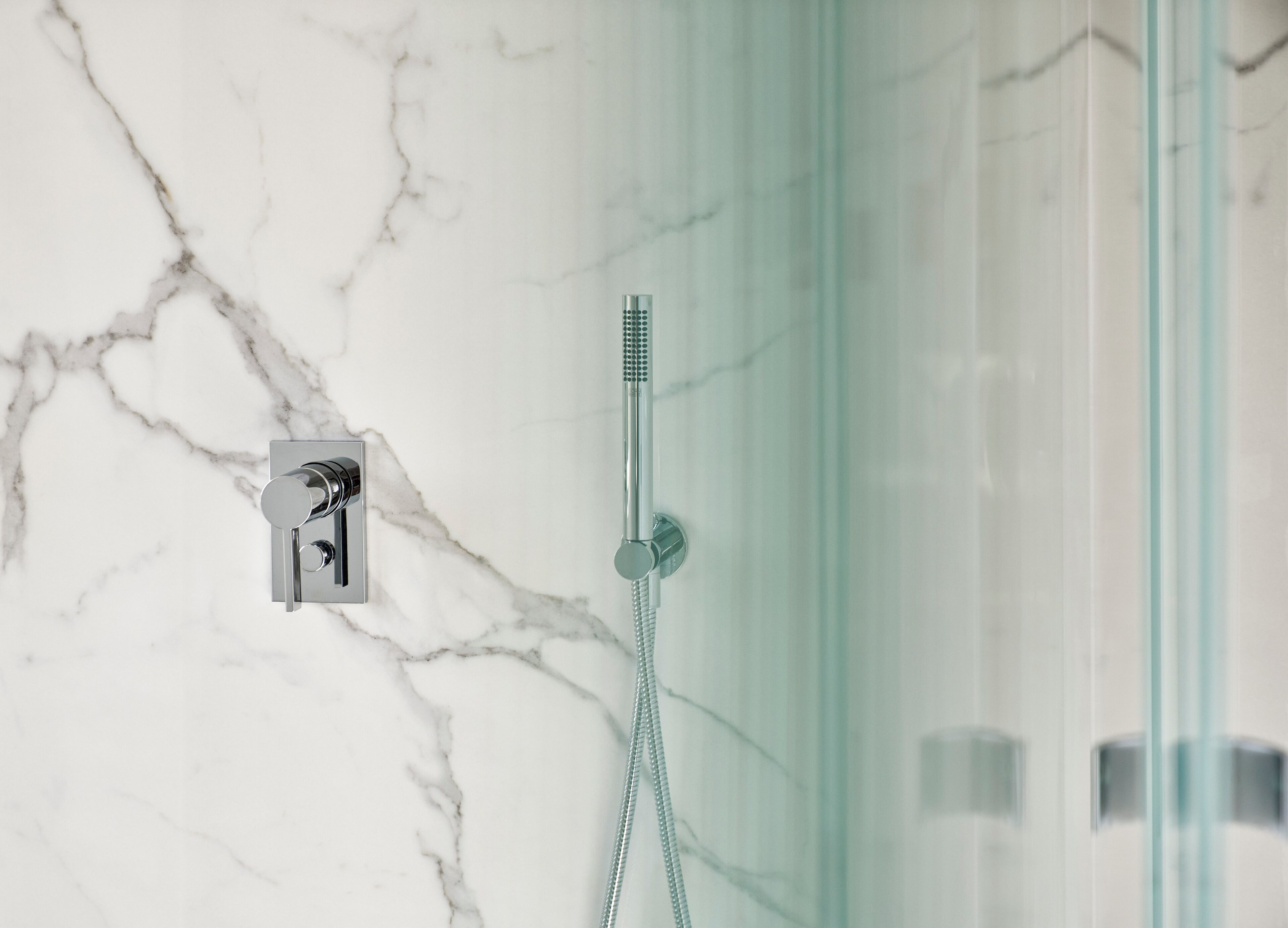 A bathroom with a marble wall, a glass shower enclosure, and a modern showerhead.