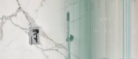 Un baño con pared de mármol, cabina de ducha de vidrio y ducha moderna.