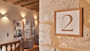 A rustic interior with a stone wall, wooden number '2' sign, and a staircase. - Hotel Le Chevalier Bleu (Monpazier)