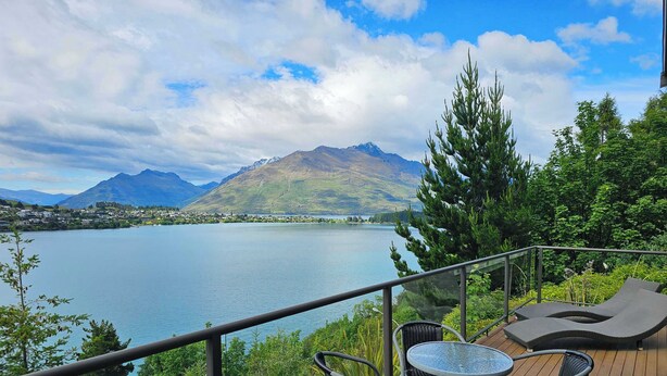Une terrasse dotée de mobilier d’extérieur, d’une balustrade en verre et offrant une vue sur un lac, avec des montagnes en arrière-plan.