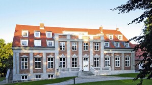 Un grand bâtiment historique à la façade symétrique, doté de nombreuses fenêtres et d’une entrée centrale surélevée par des marches.