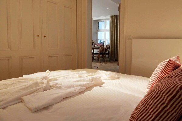 A hotel room with a neatly made bed, a dining area in the background, and a large wardrobe. - Gutshaus Zicker in Garz (Garz)
