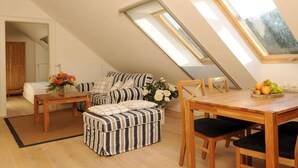 A cozy loft bedroom with a sloped ceiling, a skylight, a sofa, a dining table, and a small kitchenette. - Gutshaus Zicker in Garz (Garz)