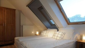 A bedroom with a sloped ceiling, a bed with white bedding, a nightstand with a lamp, and a wooden wardrobe. - Gutshaus Zicker in Garz (Garz)
