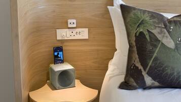 A neatly arranged bedroom with a wooden headboard, a bedside table with a smartphone charging, and a decorative pillow.