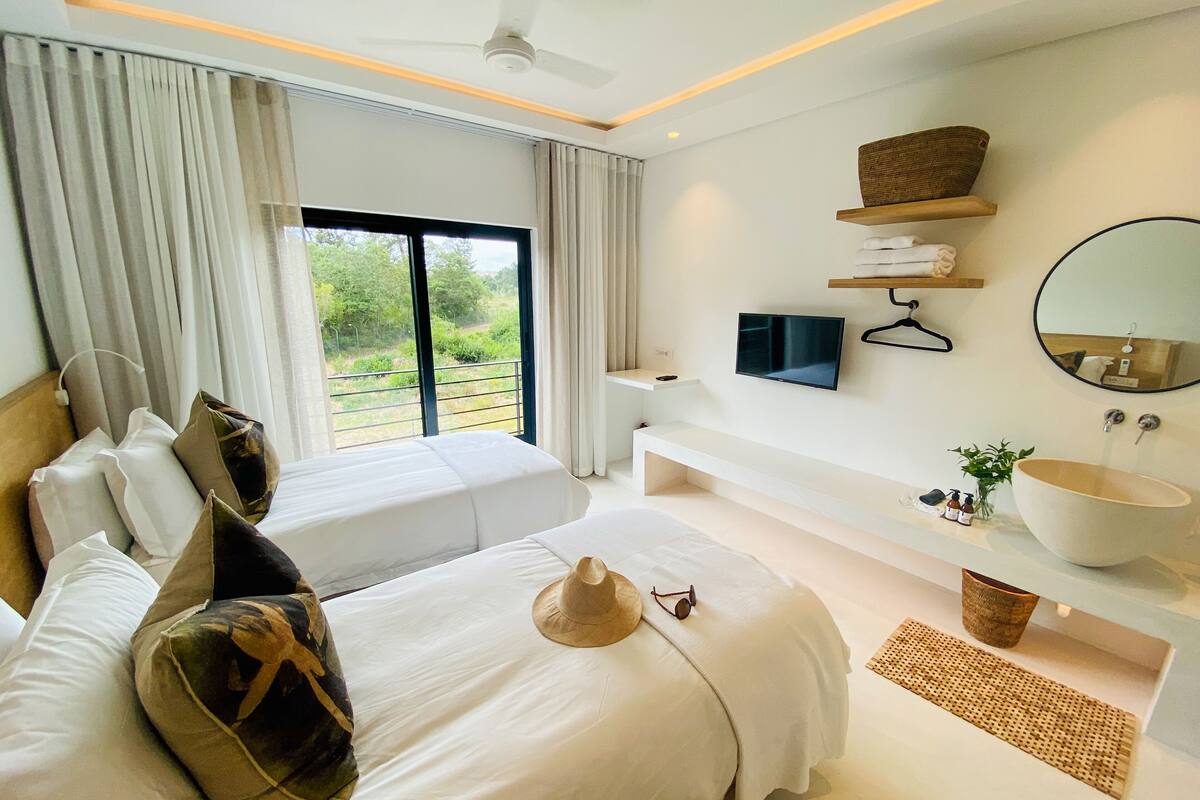 Habitación de hotel moderna con una cama grande, televisión, baño con lavamanos amplio y vistas a zonas verdes.