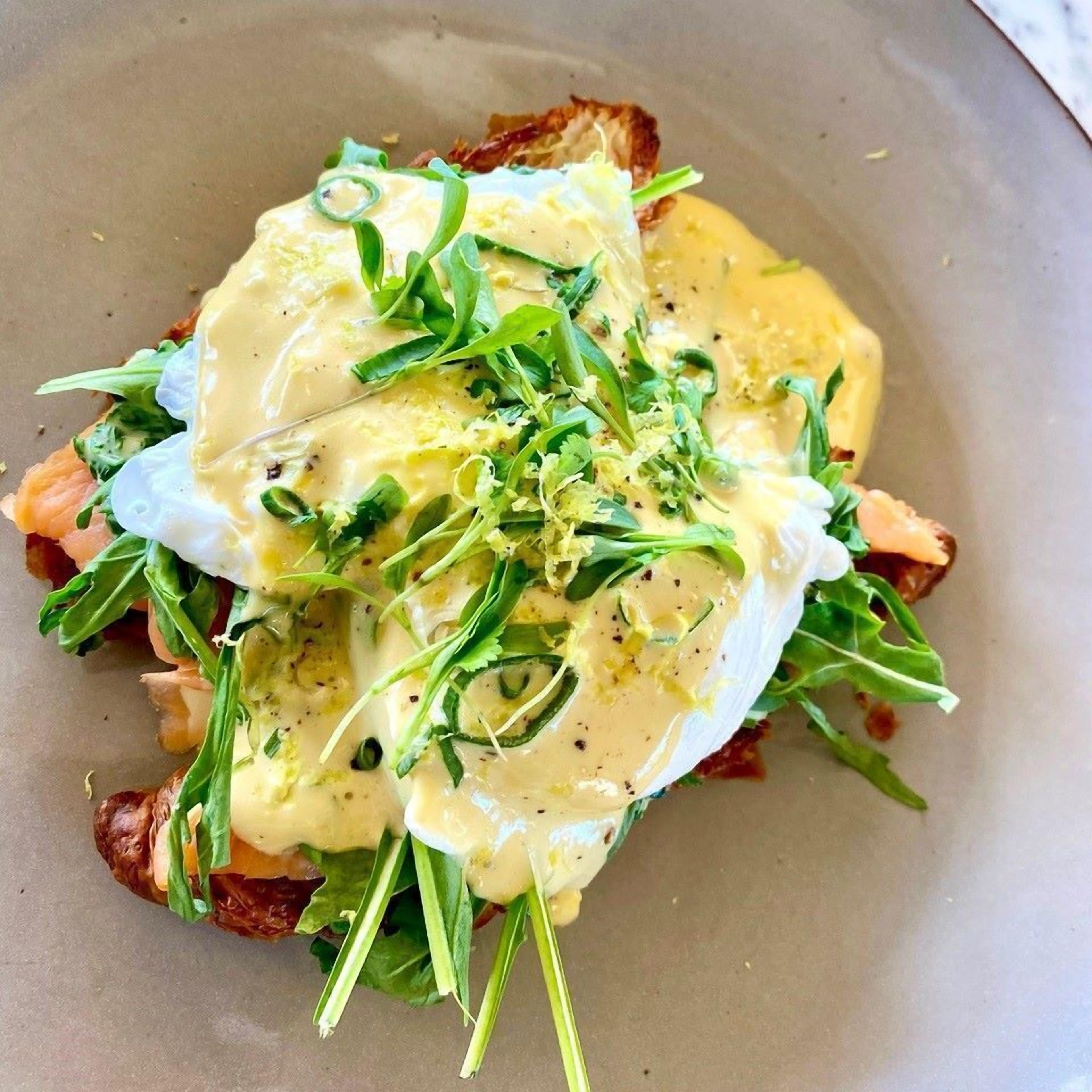 A plate with a dish consisting of toast, greens, and a poached egg with sauce.
