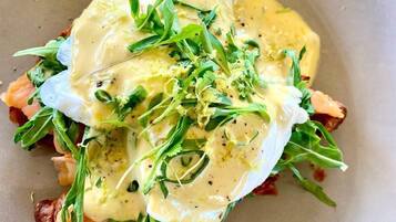 A plate with a dish consisting of toast, greens, and a poached egg with sauce.