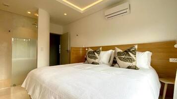 A modern hotel room with a large bed, a wooden headboard, and a glass shower enclosure.