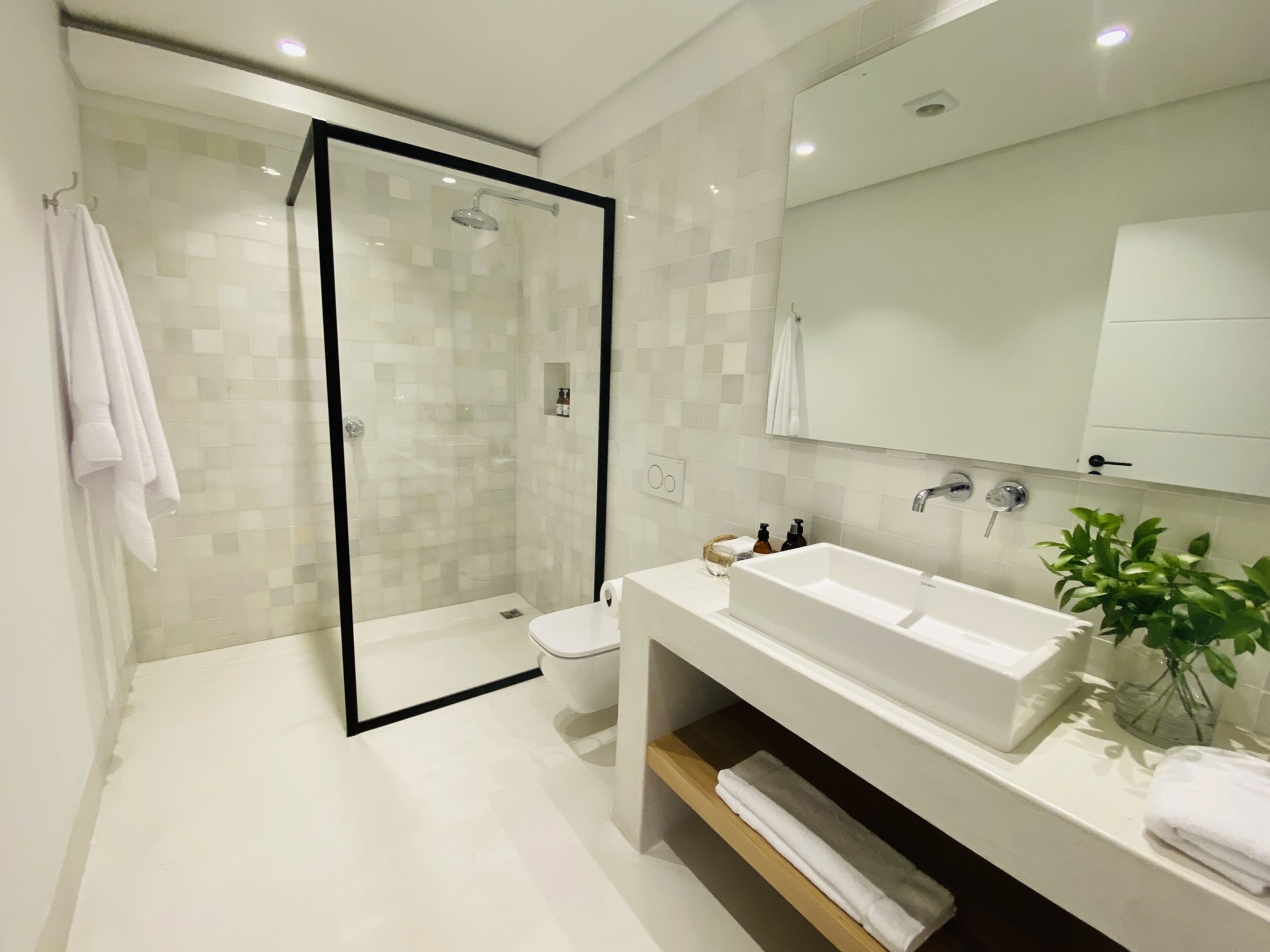 A modern bathroom with a glass-enclosed shower, a white sink, and a mirror above it.