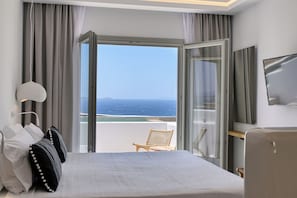 A hotel room with a large bed, a chair, a TV, and a view of the ocean. - Paola Sunset Mykonos (Mykonos)