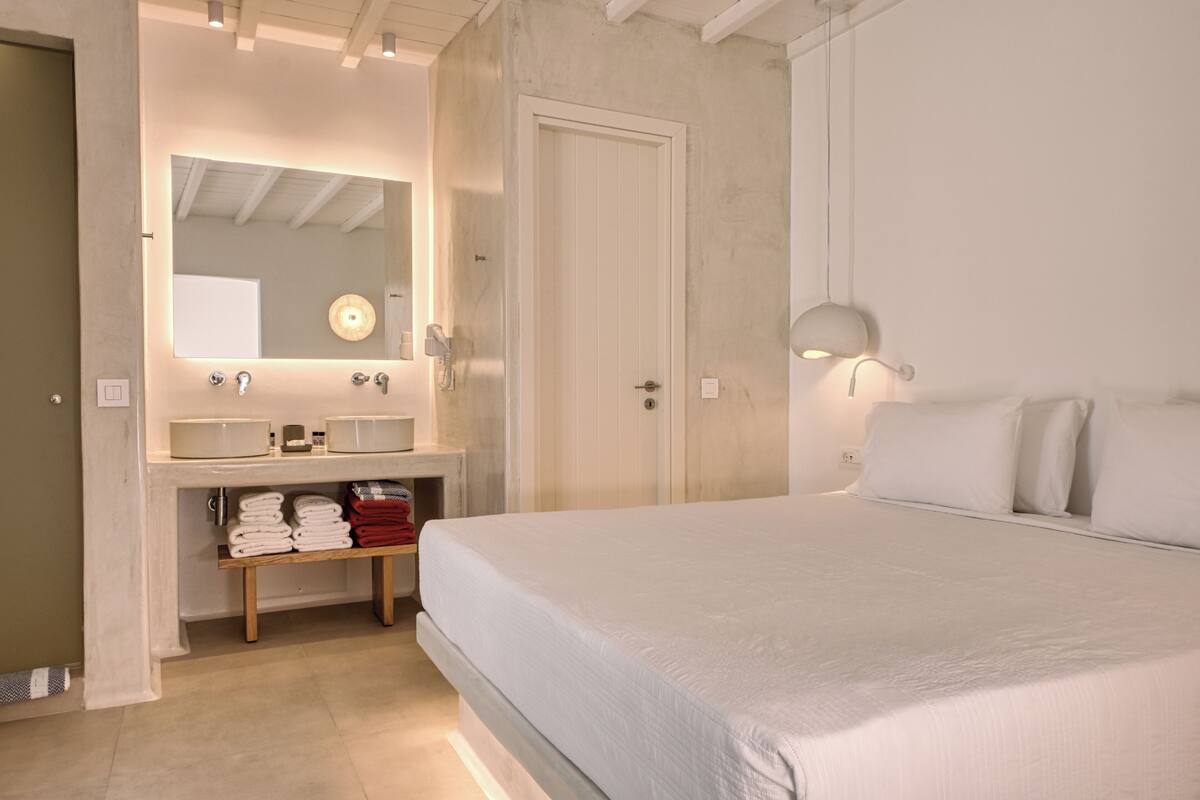 Quarto com cama, banheiro com pia e espelho, e prateleira com toalhas.