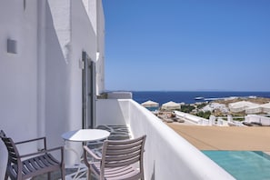 Ein Balkon mit Tisch und Stühlen, der Blick auf einen Strand und einen wolkenlosen, blauen Himmel bietet.