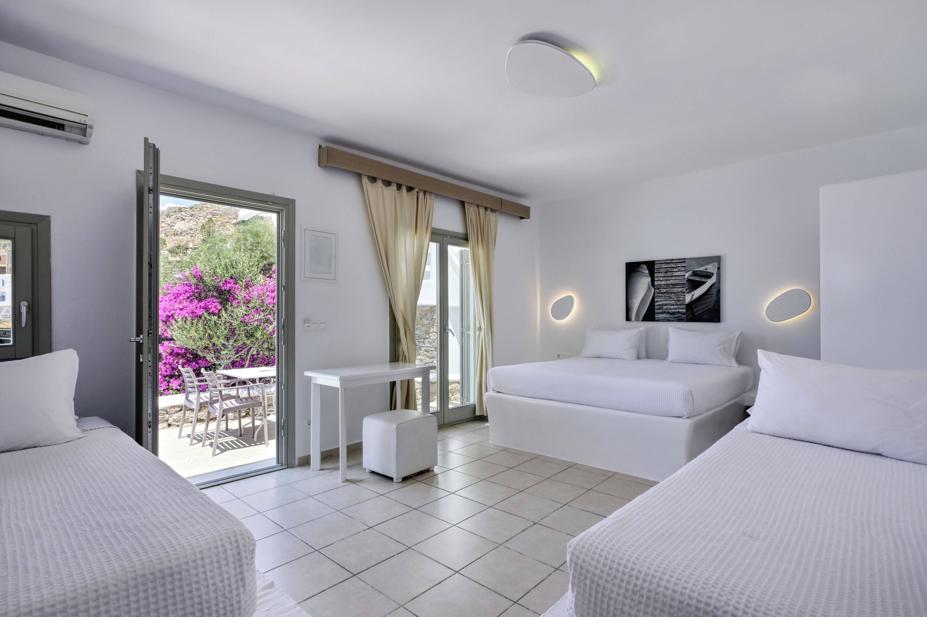 A modern hotel room with a bed, a small table, a sofa, and a view of the outdoors.