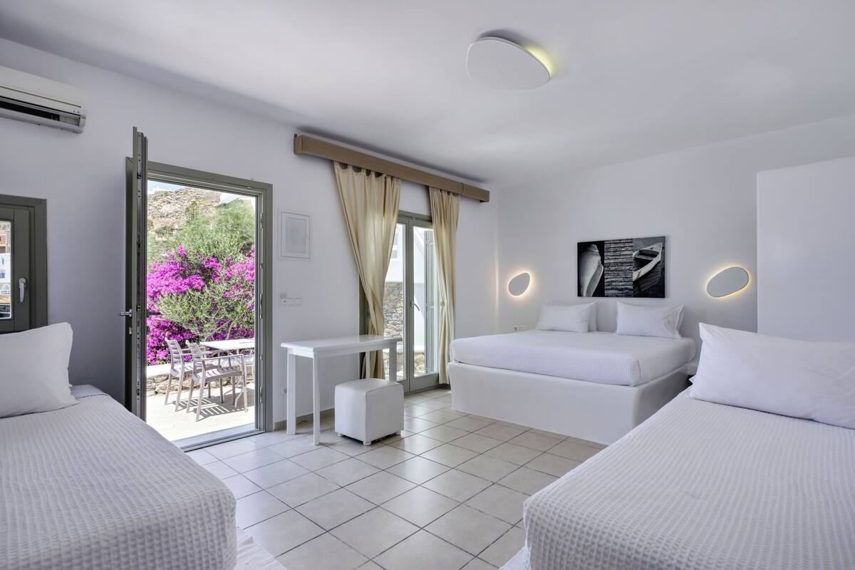 Quarto de hotel moderno com cama, mesinha, sofá e vista para o exterior.
