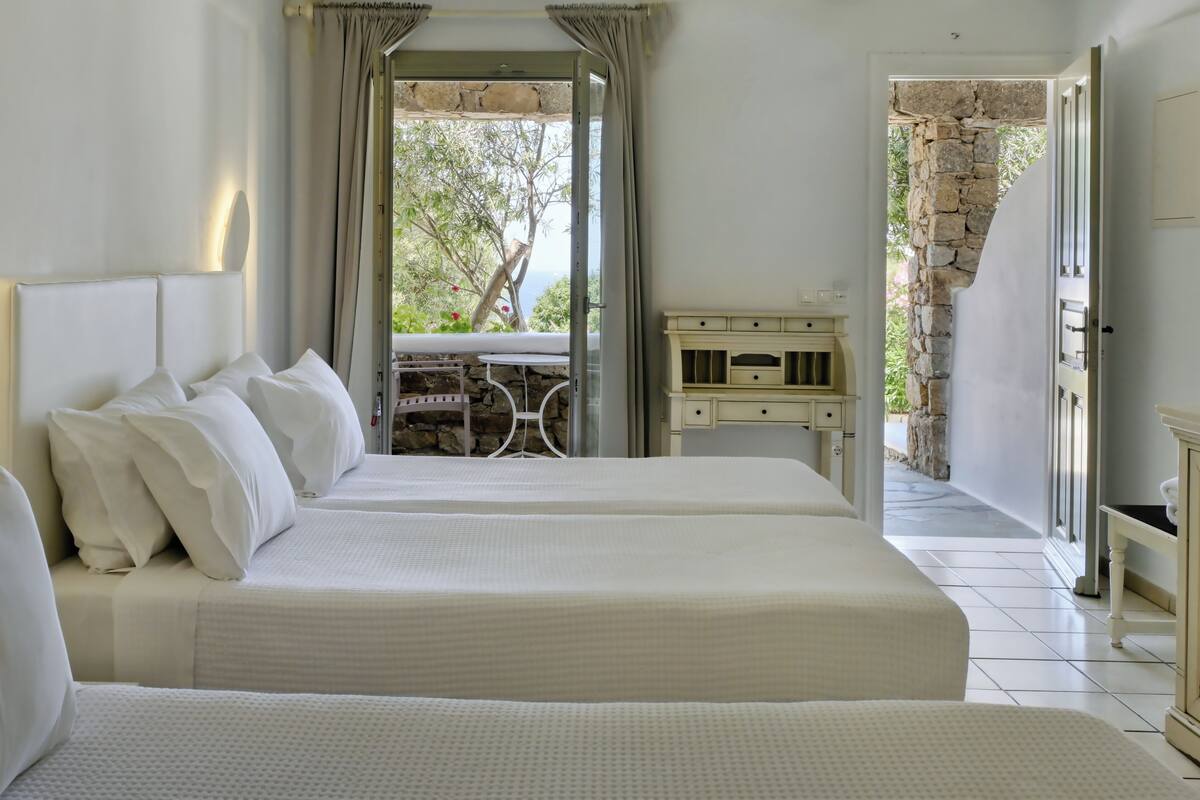 Quarto de hotel com duas camas, parede de pedra e varanda com mesa e cadeiras.