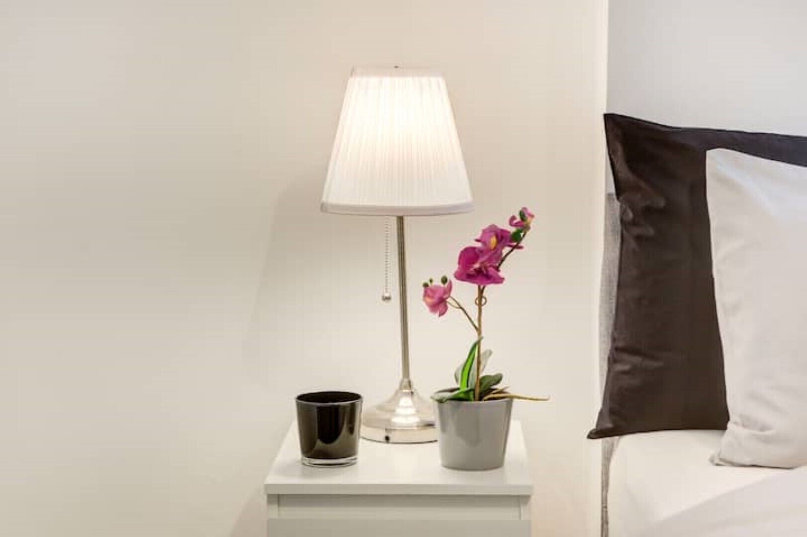 A neatly arranged bedside table with a lamp, a glass of water, and a potted orchid.