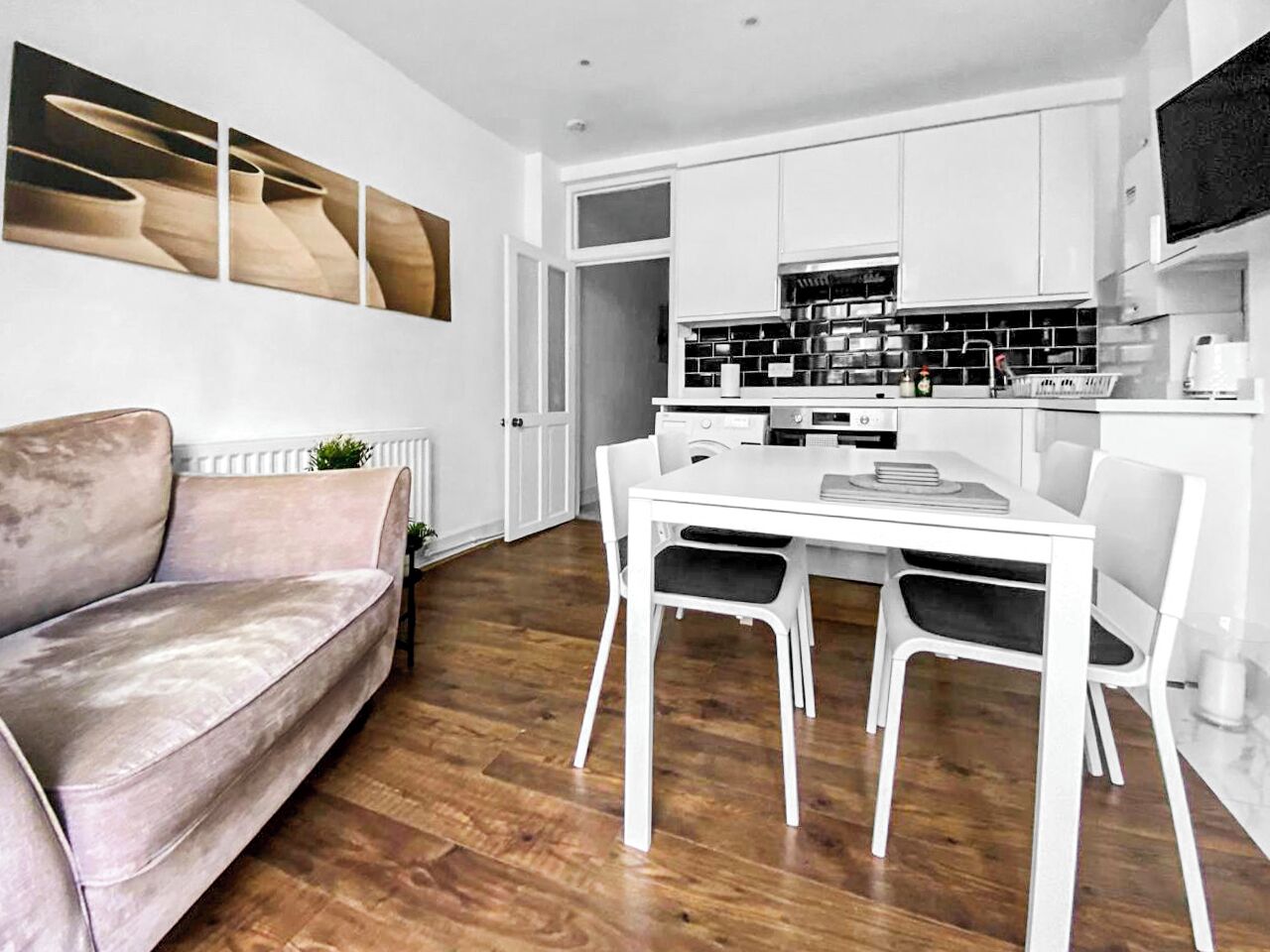 A modern kitchen with white cabinets, a dining table with four chairs, and a pink sofa.