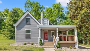 A two-story house with a front porch, a red door, and a chimney.