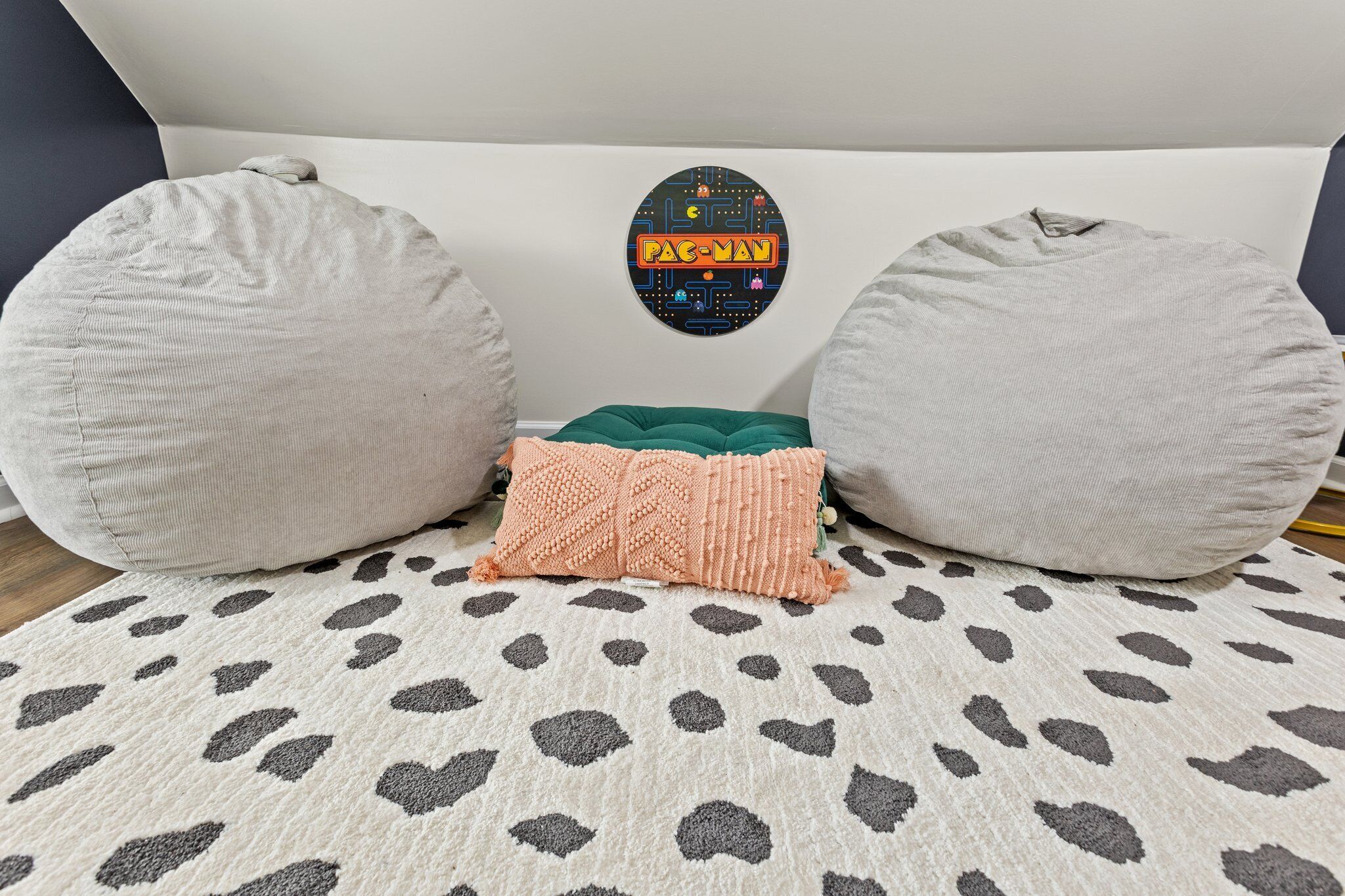 A room with a white headboard, a Pac-Man themed wall decal, and a patterned rug.