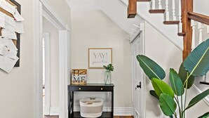 A hallway with a black console table, a corkboard with notes, a framed sign saying "YAY! you're here.", and a large plant.