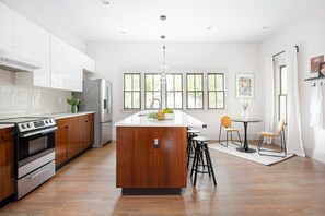 A modern kitchen with white cabinets, a central island, a built-in oven, and a dining area with a round table and stools. - Velvet Vinyl (Atlanta)