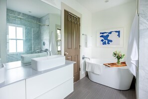 Une salle de bain moderne avec un grand miroir, deux lavabos, une baignoire et un plateau en bois posé sur la baignoire.